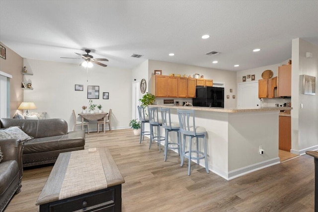 kitchen with ceiling fan, black fridge, light hardwood / wood-style flooring, and kitchen peninsula