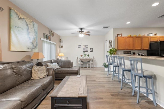 living room featuring light hardwood / wood-style flooring, ceiling fan, and a textured ceiling