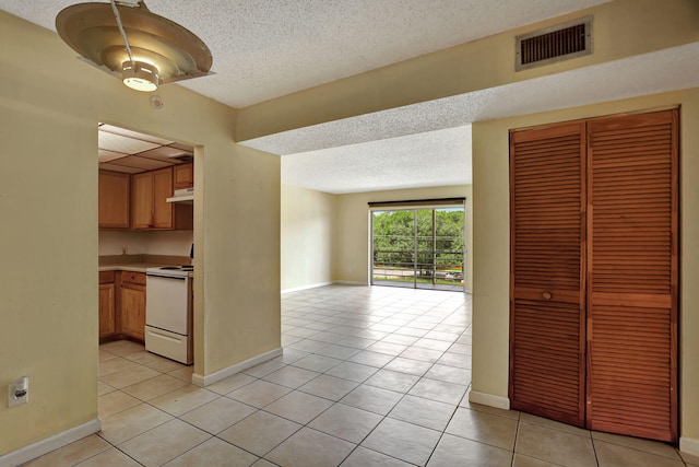 interior space featuring light tile patterned flooring, a textured ceiling, and white range with electric stovetop