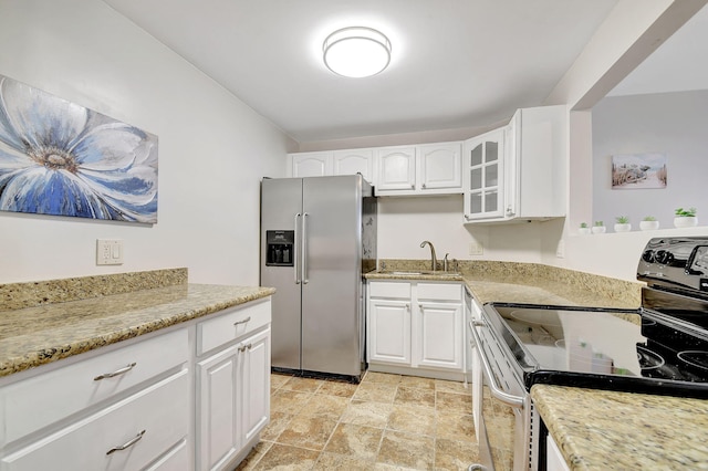 kitchen featuring stainless steel refrigerator with ice dispenser, light stone counters, sink, black electric range, and white cabinetry