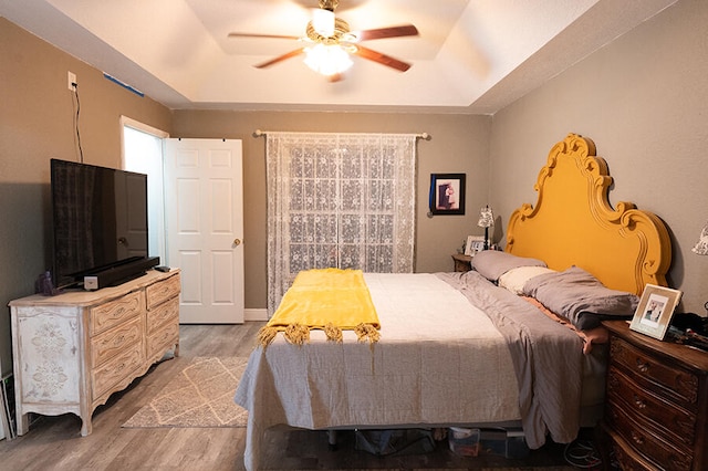 bedroom featuring ceiling fan, a tray ceiling, and wood-type flooring