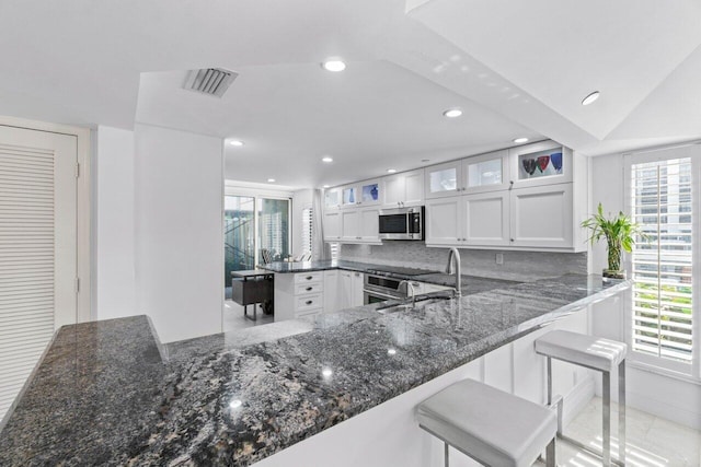 kitchen featuring a kitchen breakfast bar, kitchen peninsula, sink, white cabinets, and tasteful backsplash