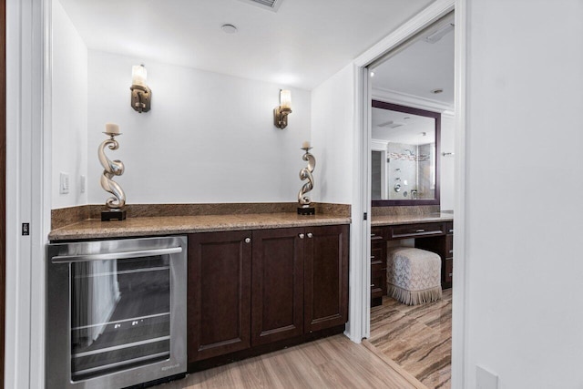 bar featuring light hardwood / wood-style flooring, dark brown cabinetry, and beverage cooler