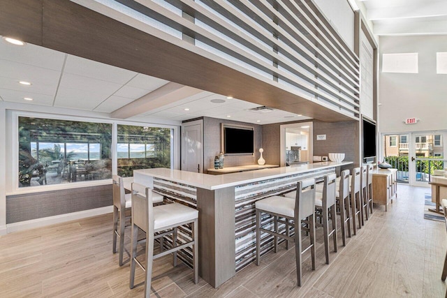 kitchen featuring kitchen peninsula, a towering ceiling, light hardwood / wood-style flooring, and a kitchen bar