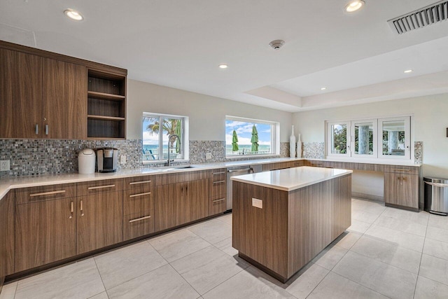 kitchen with tasteful backsplash, sink, dishwasher, a kitchen island, and light tile patterned floors