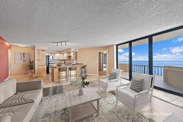 living room with a wall of windows, a textured ceiling, light tile patterned flooring, and a water view