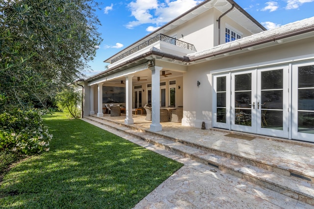 rear view of property with a lawn, ceiling fan, french doors, a balcony, and a patio