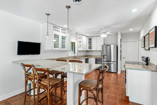 kitchen featuring white cabinets, hanging light fixtures, kitchen peninsula, appliances with stainless steel finishes, and a breakfast bar