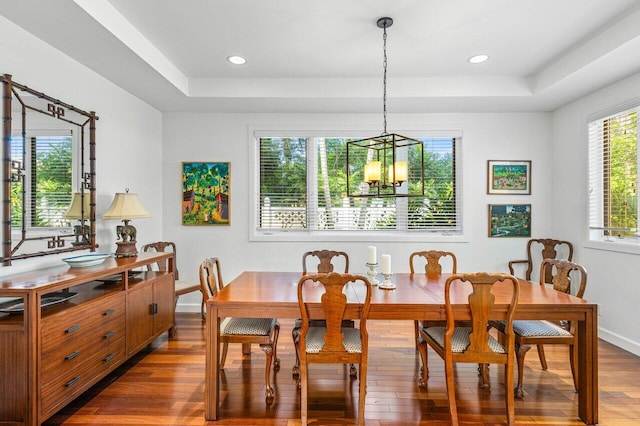 dining space featuring an inviting chandelier, a tray ceiling, and dark wood-type flooring