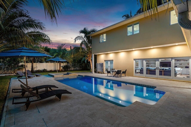 pool at dusk with a patio and a hot tub