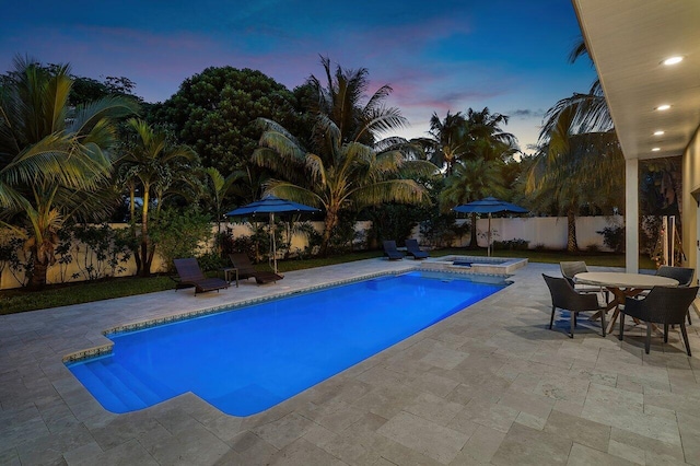 pool at dusk featuring an in ground hot tub and a patio area