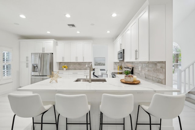 kitchen featuring sink, white cabinetry, stainless steel appliances, light stone countertops, and decorative backsplash