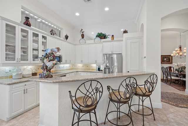 kitchen with white cabinets, light tile patterned floors, appliances with stainless steel finishes, light stone countertops, and decorative backsplash