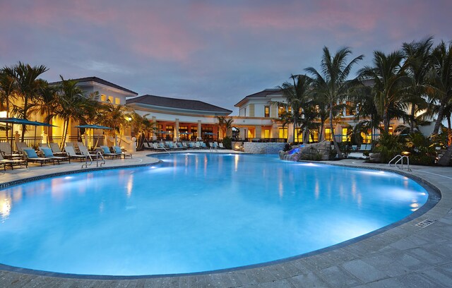 pool at dusk featuring pool water feature and a patio