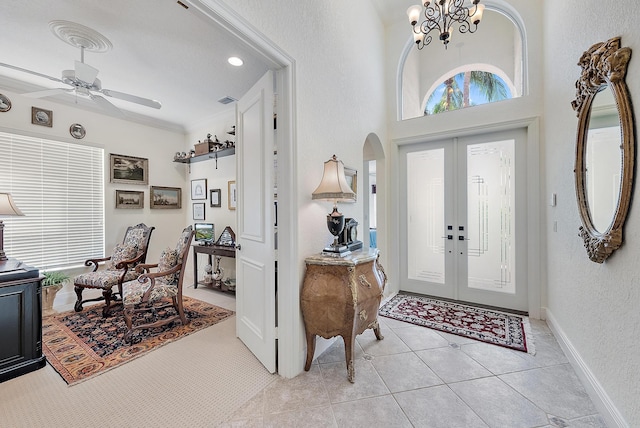 tiled entryway with french doors, ceiling fan with notable chandelier, and crown molding