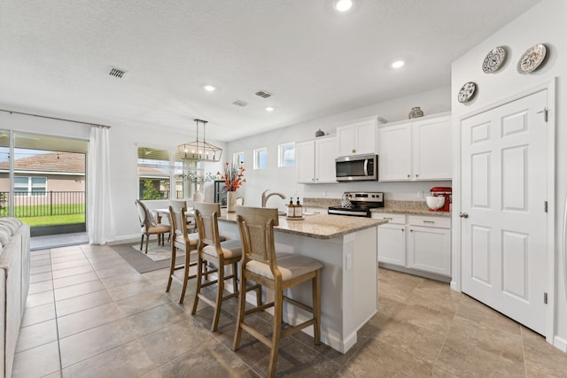 kitchen with white cabinets, hanging light fixtures, an island with sink, and appliances with stainless steel finishes