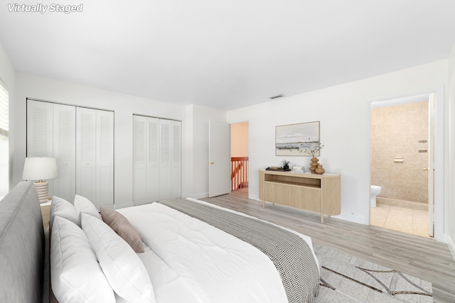 bedroom with two closets, light hardwood / wood-style flooring, and ensuite bath