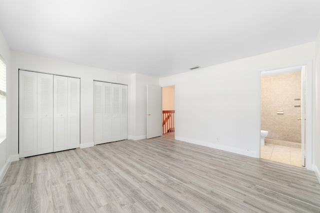 unfurnished bedroom featuring light hardwood / wood-style flooring, two closets, ensuite bathroom, and multiple windows