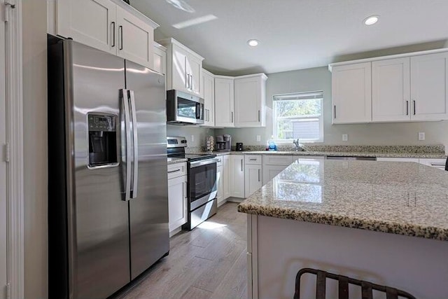 kitchen with light wood-type flooring, light stone countertops, stainless steel appliances, white cabinets, and sink