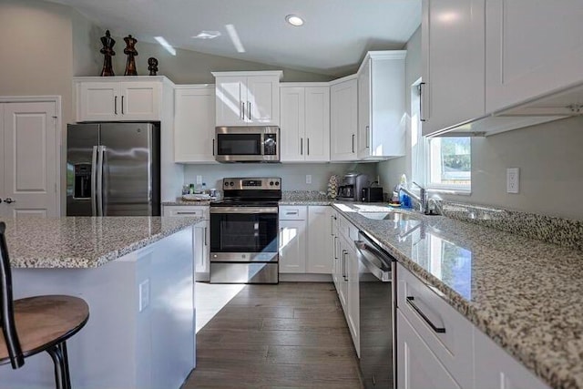 kitchen with dark hardwood / wood-style flooring, a kitchen breakfast bar, lofted ceiling, appliances with stainless steel finishes, and white cabinetry