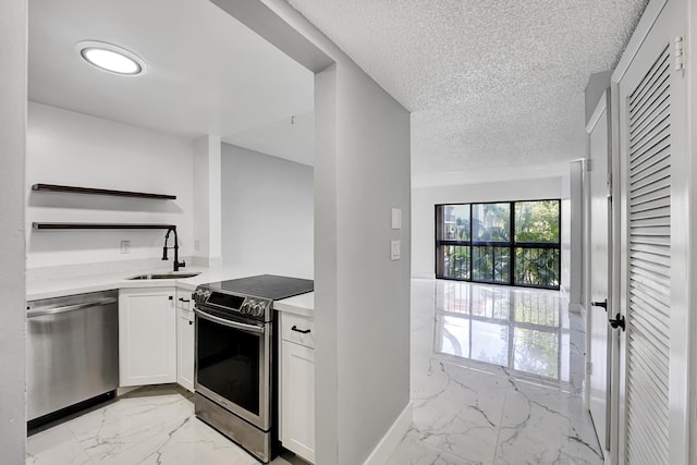 kitchen with appliances with stainless steel finishes, a textured ceiling, white cabinetry, and sink