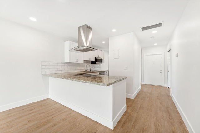 kitchen with white cabinetry, island exhaust hood, decorative backsplash, kitchen peninsula, and light wood-type flooring