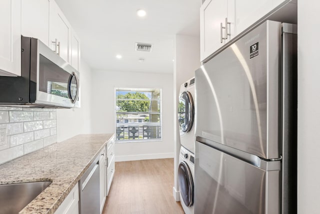 kitchen with white cabinetry, stainless steel appliances, stacked washer / dryer, light stone counters, and decorative backsplash