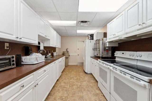 kitchen with sink, a drop ceiling, light tile patterned floors, white appliances, and white cabinets