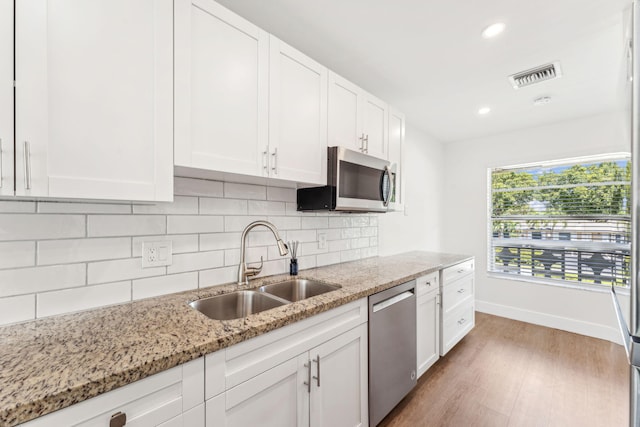 kitchen with sink, stainless steel appliances, light stone countertops, decorative backsplash, and white cabinets