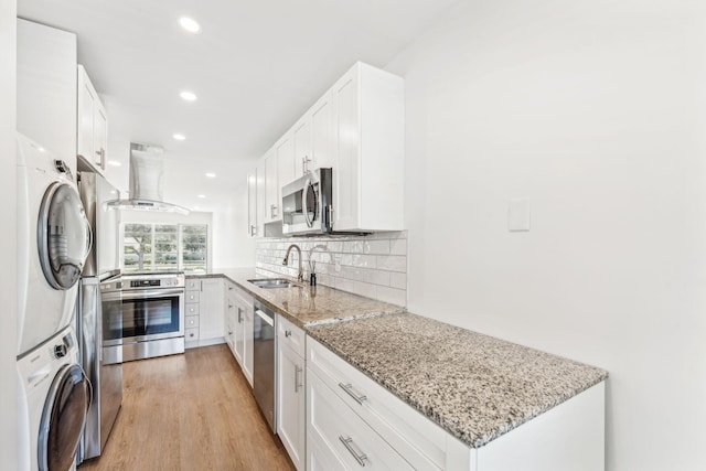 kitchen with sink, white cabinets, stacked washer / drying machine, stainless steel appliances, and light stone countertops