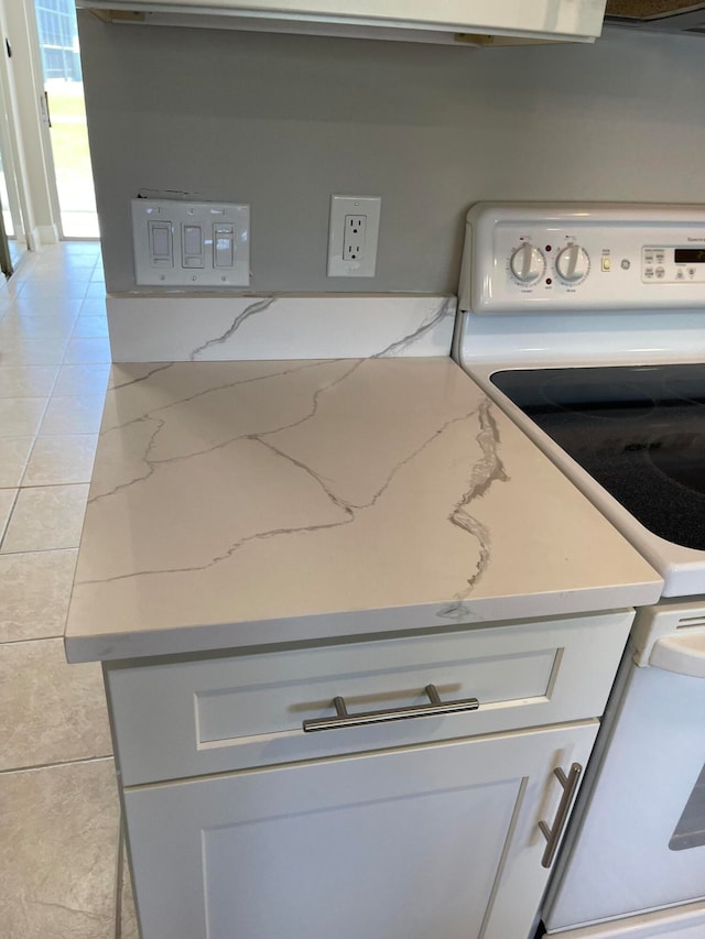 room details featuring white cabinetry, light tile patterned flooring, light stone counters, and white electric stove