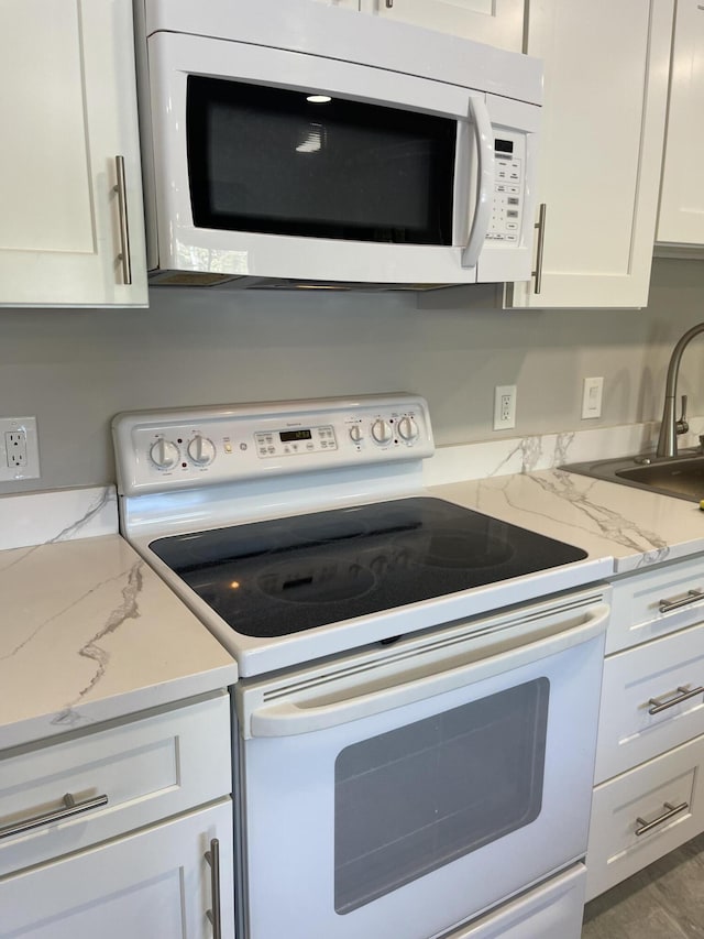 kitchen with white appliances, white cabinetry, light stone countertops, and a sink