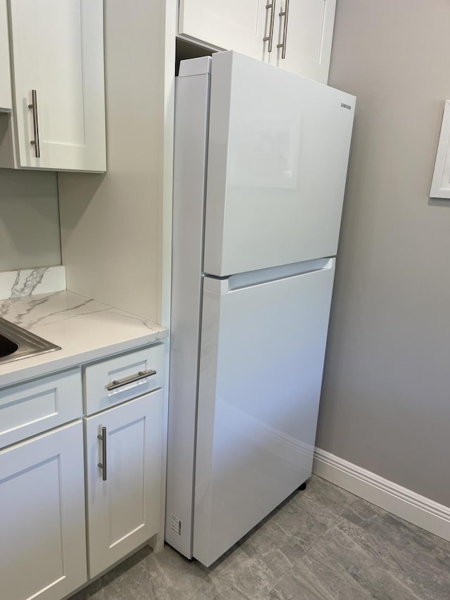 kitchen featuring baseboards, freestanding refrigerator, and white cabinets