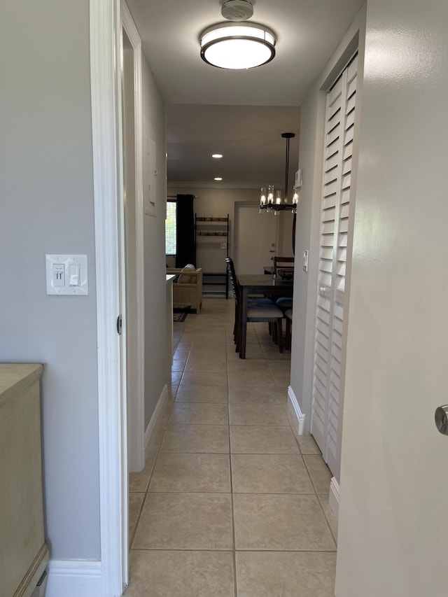 corridor with light tile patterned flooring, baseboards, and a chandelier