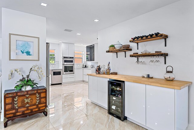 bar with tasteful backsplash, butcher block counters, white cabinets, wine cooler, and stainless steel double oven