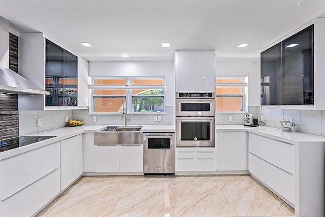 kitchen with sink, double oven, white cabinets, black electric stovetop, and wall chimney range hood