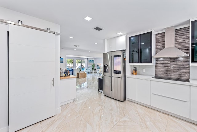 kitchen featuring white cabinetry, stainless steel refrigerator with ice dispenser, black electric stovetop, a barn door, and wall chimney exhaust hood