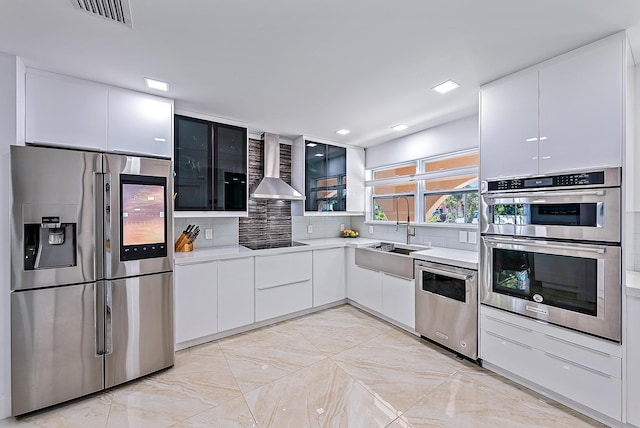 kitchen featuring wall chimney range hood, sink, white cabinetry, backsplash, and stainless steel appliances