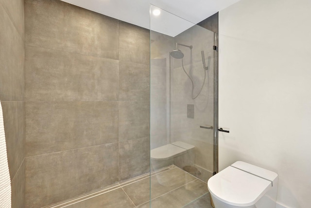 bathroom with tiled shower, toilet, and tile patterned flooring