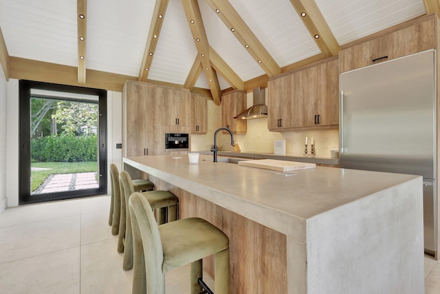 kitchen with a spacious island, appliances with stainless steel finishes, wall chimney exhaust hood, and lofted ceiling with beams