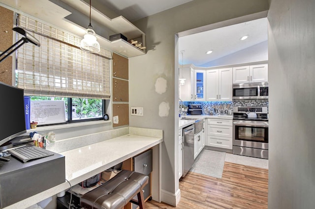 kitchen with pendant lighting, lofted ceiling, light wood-type flooring, white cabinetry, and stainless steel appliances