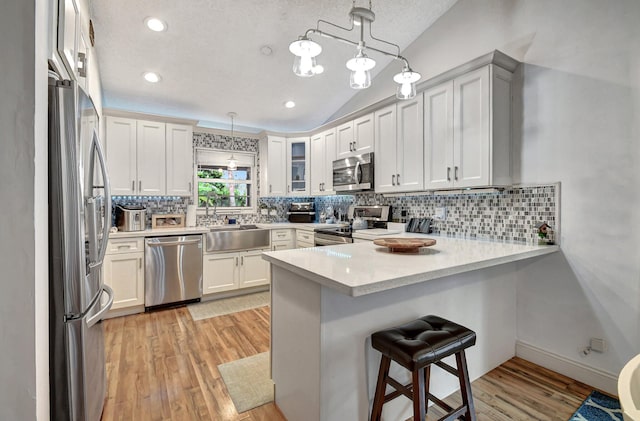 kitchen with a textured ceiling, appliances with stainless steel finishes, decorative light fixtures, light hardwood / wood-style floors, and kitchen peninsula