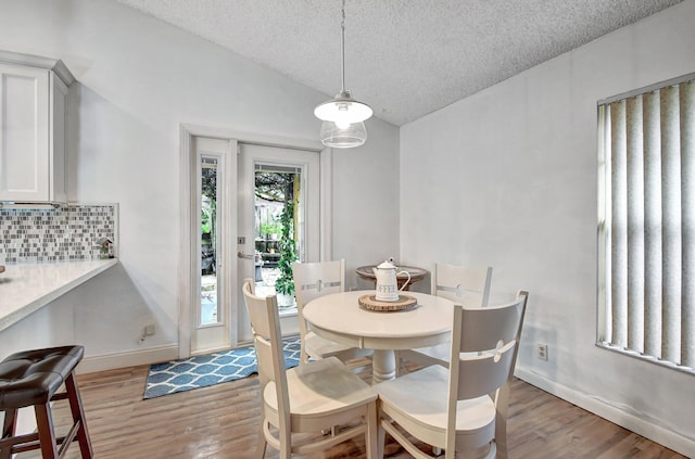 dining space with light wood-type flooring, a textured ceiling, and lofted ceiling