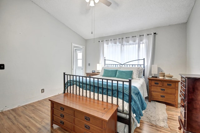 bedroom featuring a textured ceiling, light hardwood / wood-style floors, vaulted ceiling, and ceiling fan