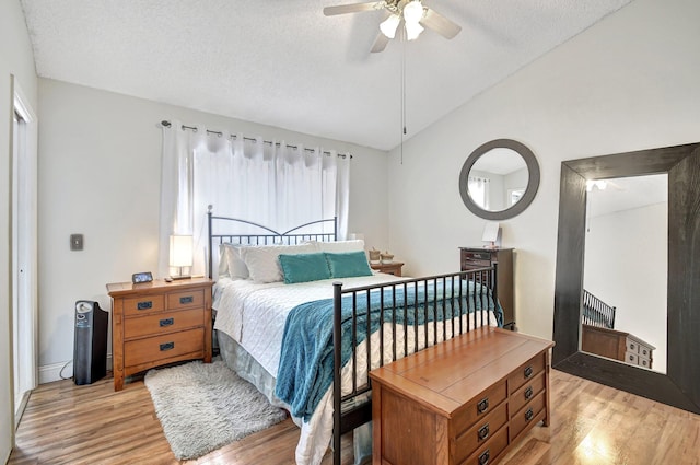 bedroom with a textured ceiling, ceiling fan, light hardwood / wood-style floors, and lofted ceiling