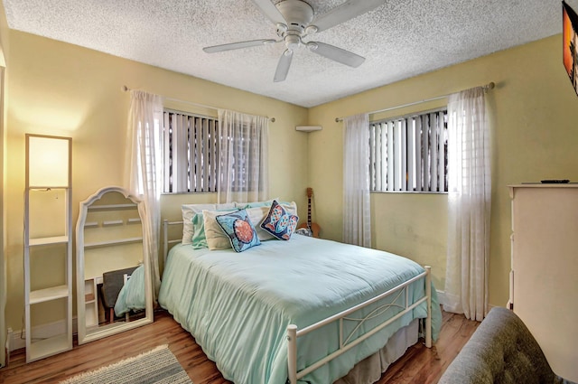 bedroom with multiple windows, wood-type flooring, a textured ceiling, and ceiling fan