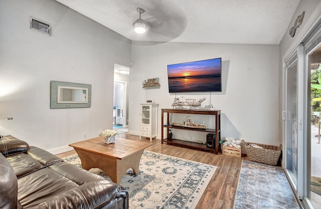 living room with a textured ceiling, hardwood / wood-style flooring, vaulted ceiling, and ceiling fan