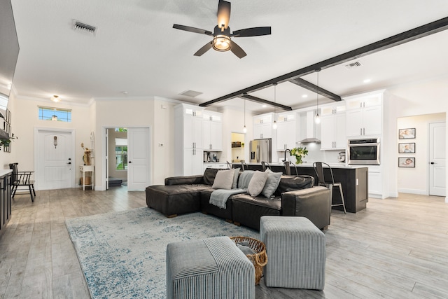 living room with ceiling fan, ornamental molding, light hardwood / wood-style flooring, and beam ceiling