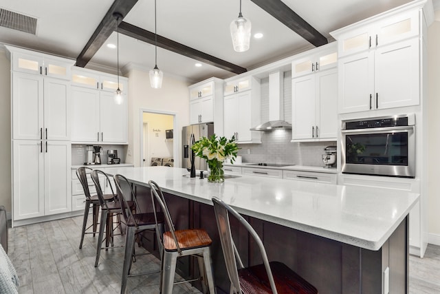 kitchen featuring white cabinets, beamed ceiling, a large island, wall chimney range hood, and stainless steel appliances