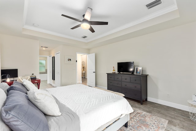 bedroom with ornamental molding, light wood-type flooring, a tray ceiling, and ceiling fan